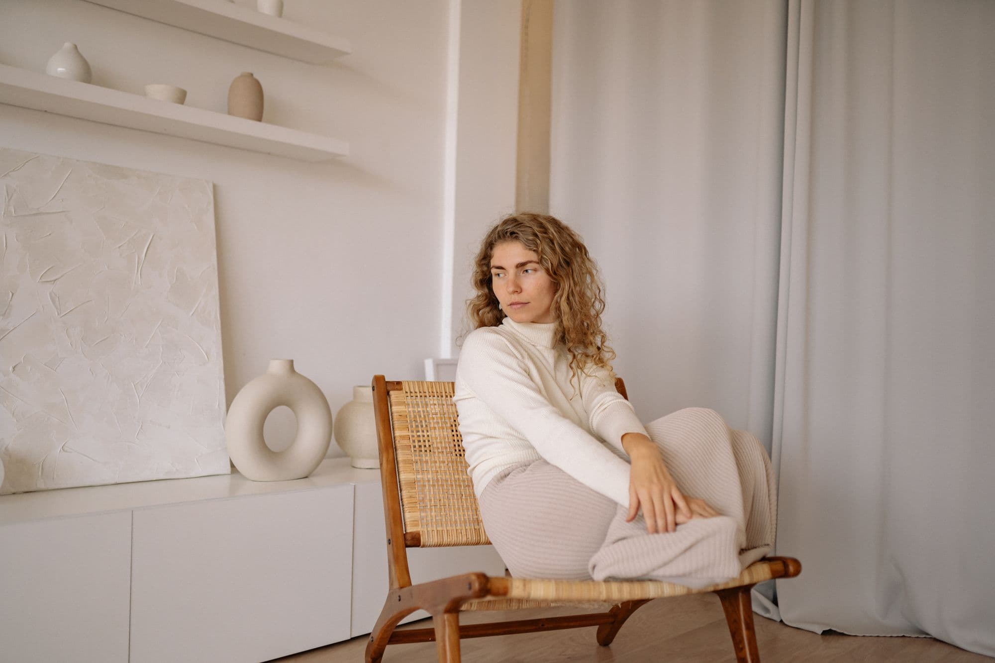 Woman in linen sitting on a woven chair in a bright, calm room